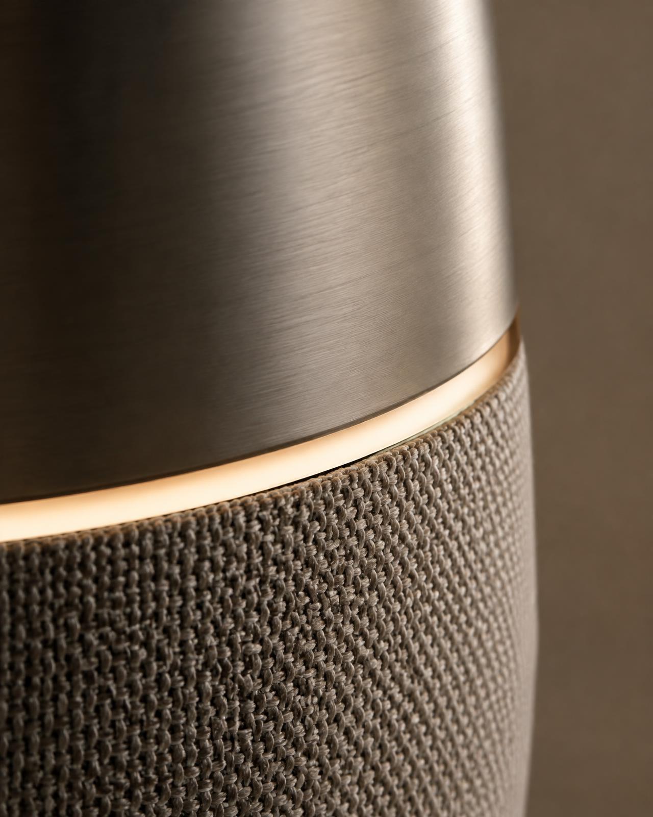 Close-up: brushed aluminum meeting woven warm-gray fabric, separated by a thin glowing light ring.